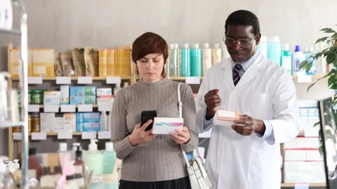 Woman in pharmacy scans QR code on pills. African man pharmacist in background Stock Footage 327129516