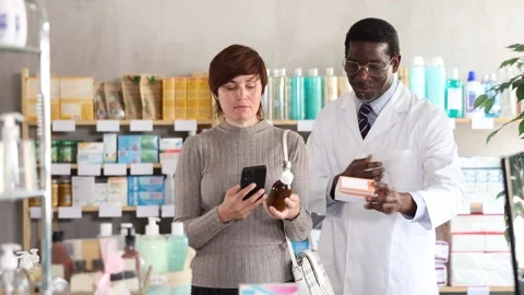 Woman in pharmacy scans QR code on antitussive syrup. African man pharmacist in Stock Footage 327694820
