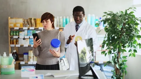 Woman in pharmacy scans QR code on infant formula. African man pharmacist in Stock Footage 328135139
