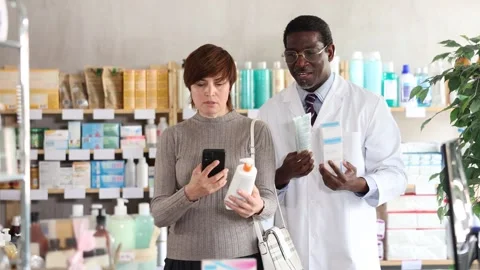 Woman in pharmacy scans QR code on body cream. African man pharmacist in Stock Footage 329393059
