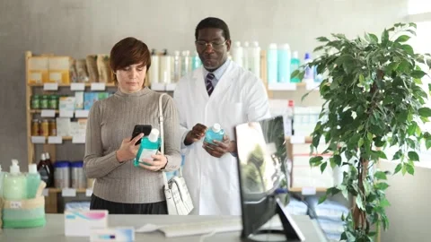 Woman in pharmacy scans QR code on mouthwash. African pharmacist in background Stock Footage 331297168