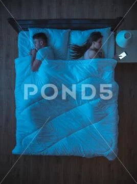 The woman phone on the bed near the husband. night time. view from above Stock Photos