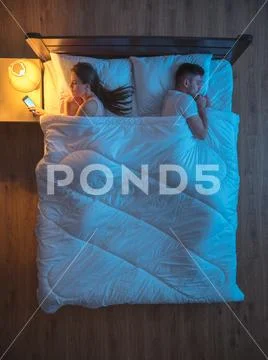 The woman phone on the bed near the husband. night time. view from above Stock Photos