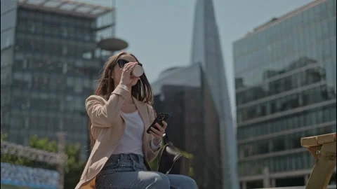 Woman with phone drinking coffee while standing between business buildings Stock Footage 253512005