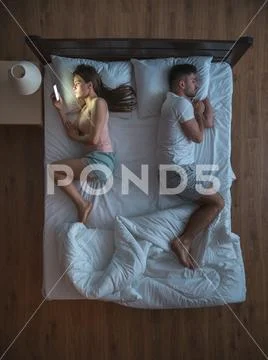 The woman with phone lay on the bed near husband. view from above Stock Photos