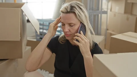 Woman on phone touching forehead while holding smartphone amid packed cardb.. Stock Footage 339255558