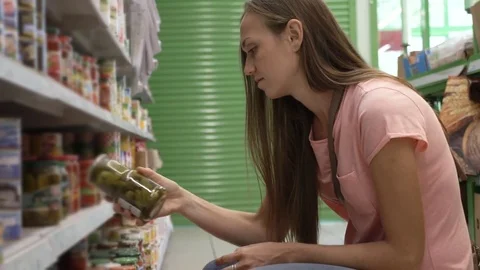 Woman picking canned food from the shelves at supermarket and reading the label Stock Footage