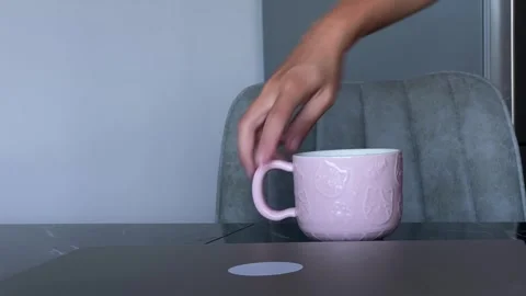 Woman picking up ceramic mug close-up from table beside dining chair Stock Footage 345361802