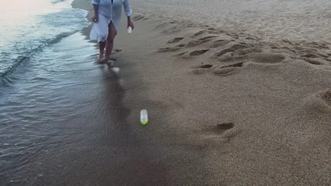 Woman picking up plastic bottle from sandy beach near sea water. Beach cleanup Stock Footage 337412099