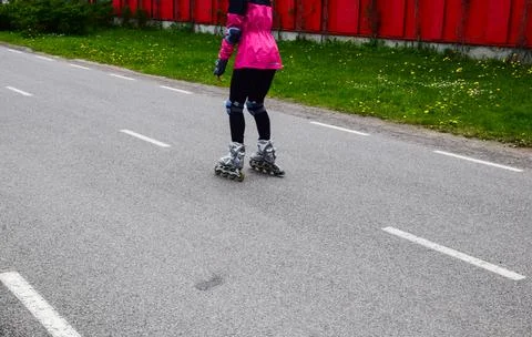 Woman in pink jacket rollerblading on an empty asphalt road with green grass Stock Photos