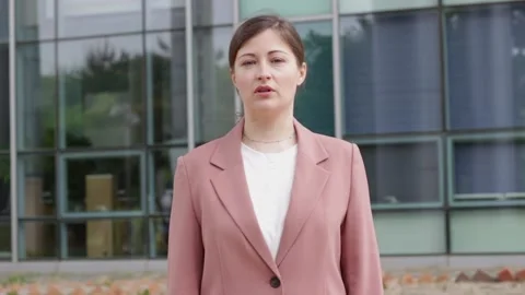 Woman in pink jacket talking on background of an office building. Stock Footage 153445740