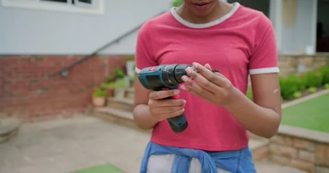 Woman in pink tee checking, inserting bit in cordless drill, drilling hole in Stock Footage 338326329