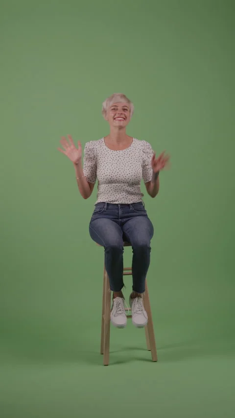 A Woman with a Pixie Haircut Waves with Both Hands in Front of Green Background Video stock 211869168