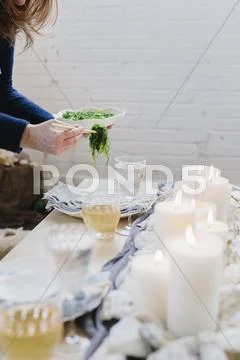 A woman placing a plate of food on a table decorated with lighted candles. Stock Photos
