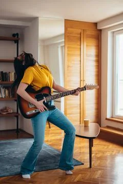 Woman playing guitar while dancing and singing in her living room at home Stock Photos