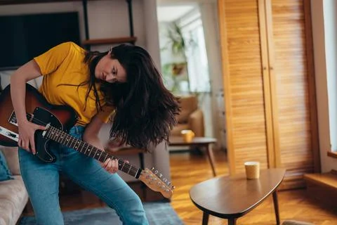 Woman playing guitar while dancing and singing in her living room at home Stock Photos