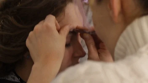 Woman plucks the eyebrows of a young pretty model with a beautiful hairstyle Stock Footage