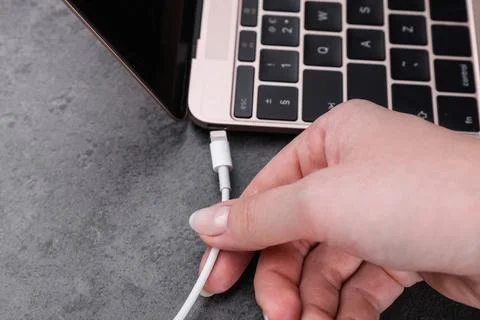 Woman plugging USB cable with lightning connector into laptop port on dark .. Stock Photos
