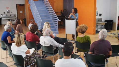 Woman At Podium Chairing Neighborhood Meeting In Community Centre Stock Footage