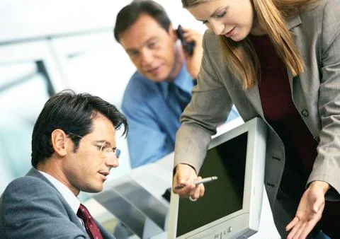 Woman pointing to computer screen, man sitting in front of computer, second man Foto stock