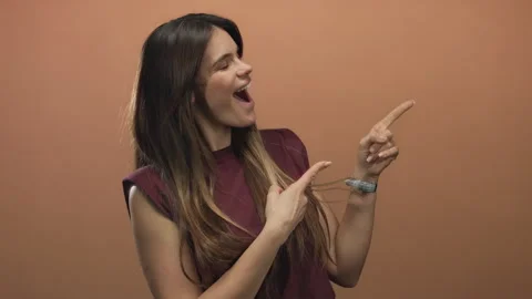Woman points with joy against a solid brown background, wearing casual atti.. Stock Footage 314634325