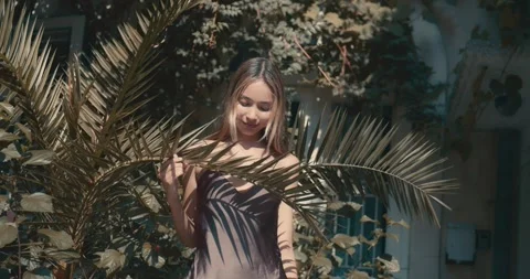 A woman is posing in front of a palm tree, holding a leaf in her hand Stock-Footage 283823717