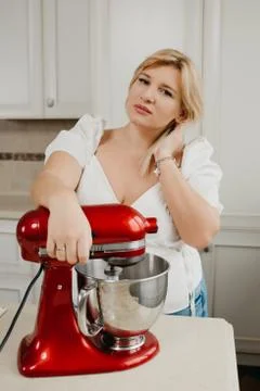 A woman is posing leaning on a red stand mixer during it is whipping ingredie Stock Photos
