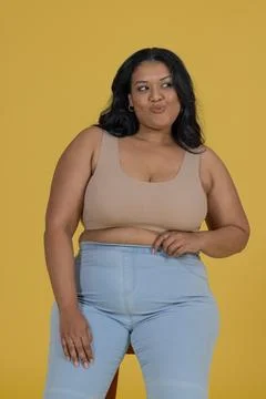 Woman posing on low stool in studio mustard backdrop croptop jeans hoops Stock Photos