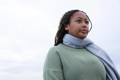 Woman posing outside under cloudy sky, wearing green knit, gray scarf, showing Stock Photos