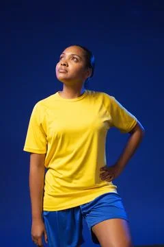 Woman posing in studio against deep blue backdrop wearing yellow athletic tee Stock Photos