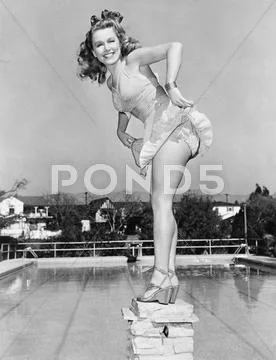 Woman posing on top of a pillar next to a swimming pool Stock Photos