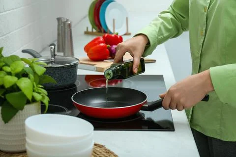 Woman pouring cooking oil from bottle into frying pan in kitchen, closeup Stock Photos