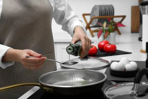 Woman pouring cooking oil from bottle into frying pan in kitchen, closeup Stock Photos