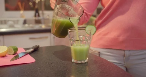 Woman pouring green juice into a glass in a bright kitchen. Stock Footage