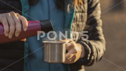 Woman is pouring hot drink from thermos into travel mug