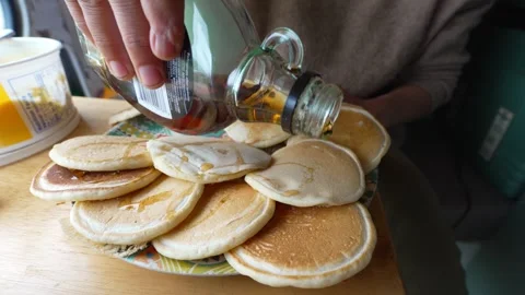 Woman pouring maple syrup on a stack of pancakes for breakfast in a camper van Stock Footage 342131906