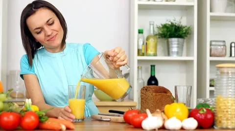 Woman pouring orange juice into a glass and drink Stock Footage