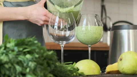 A woman pours a green cocktail into transparent glasses. Fitness and diet. The c Stock Footage