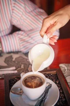 Woman pours milk into coffee from a white container Stock Photos