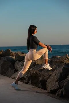 Woman practices stretching exercise on large rocks ocean's edge during sunset Stock Photos