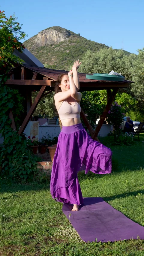 Woman practicing eagle arms tree pose in a scenic village garden Stock Footage 336146241