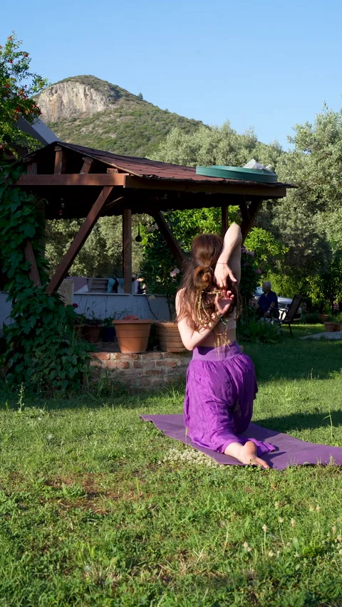Woman practicing reverse prayer yoga pose in a scenic village garden Stock-Footage 336146755