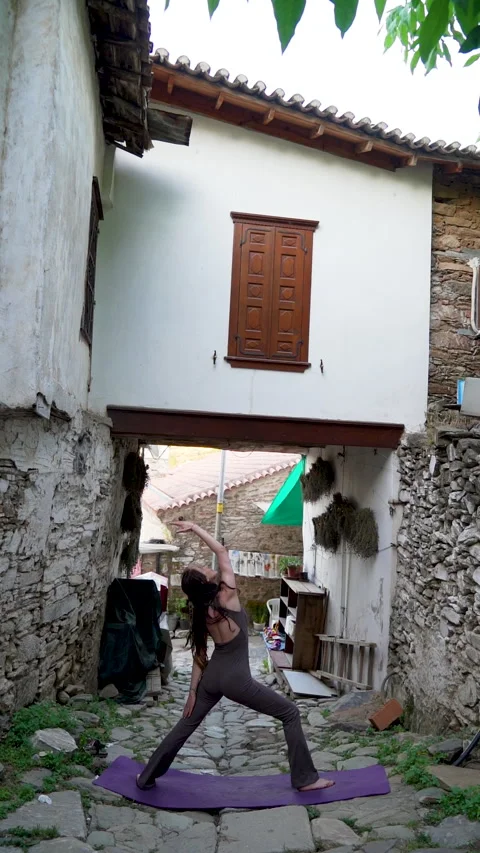 Woman practicing reverse warrior yoga pose in historic Sirince village Stock Footage 336135676