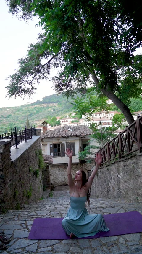 Woman practicing seated eagle pose yoga on a historic village street Stock Footage 336165912