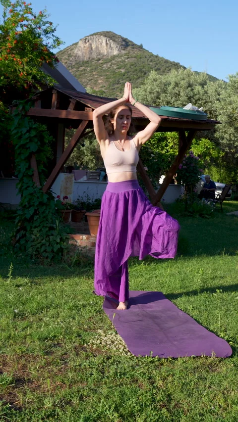 Woman practicing tree yoga pose in a scenic village garden Video stock 336127344