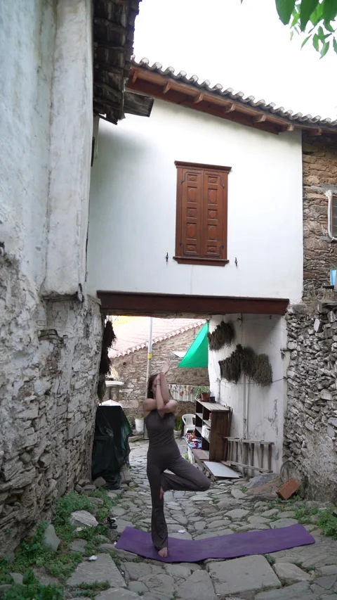 Woman practicing tree yoga pose in historic Sirince village street Vidéo 336164004
