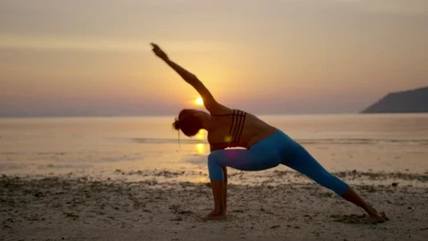 Woman practicing triangle pose on the beach during sunset Stock Footage 75286663
