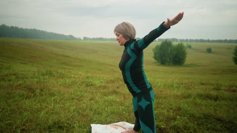 Woman practicing triangle pose in open field with arms extended under cloudy sky Stock Footage 289082826