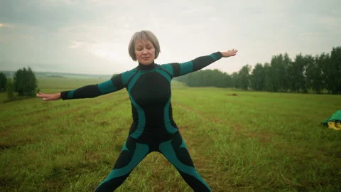 Woman practicing triangle yoga pose in open grassy field under cloudy sky Stock Footage 291471861