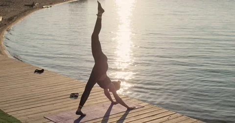 Woman is practicing yoga in down facing dog pose on one leg on river pier. Stock Footage 138396290